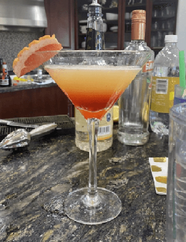 Orange and Red drink in a martini glass with a grapefruit garnish