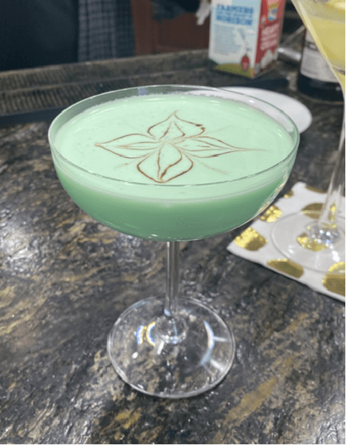 Signature green creamy cocktail in a coupe glass with a fancy gold design on top