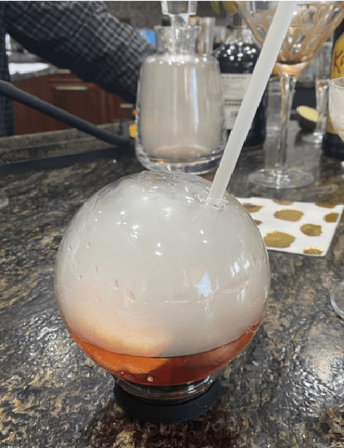 Round cocktail with a straw in front of a champagne flute