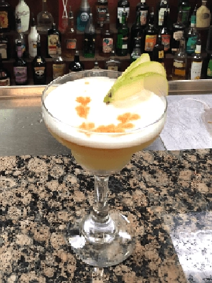 Foamy ginger cocktail in a martini glass with a piece of sugared ginger as a garnish