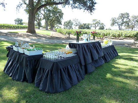 Tables with white table cloths and black skirts, set with wine and champagne glasses at an event in Plano